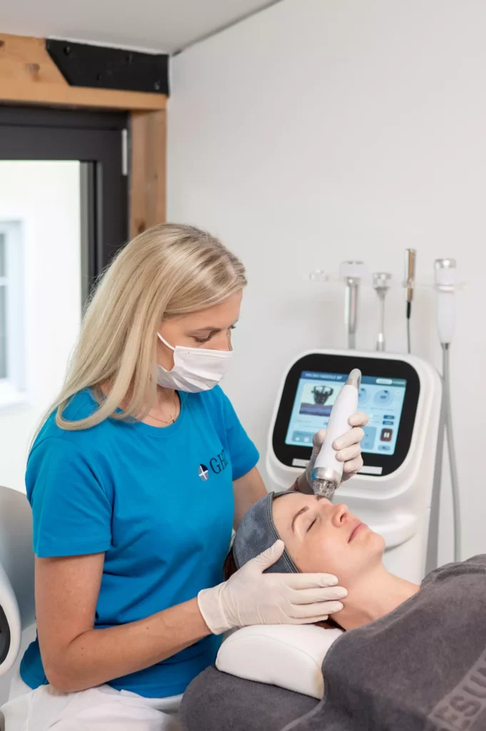 Kosmetikerin mit Maske behandelt Frau im Gesundheitszentrum Radstadt mit moderner Hautpflegegerät am Gesicht