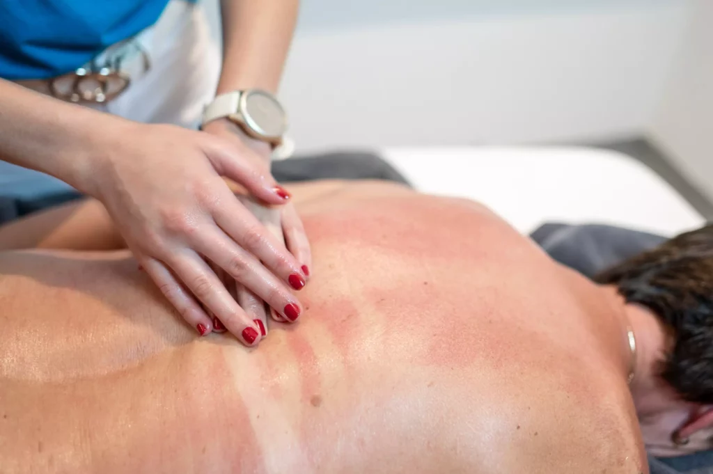 Massage im Gesundheitszentrum Radstadt mit Händen und rotem Nagellack auf dem Rücken eines liegenden Patienten