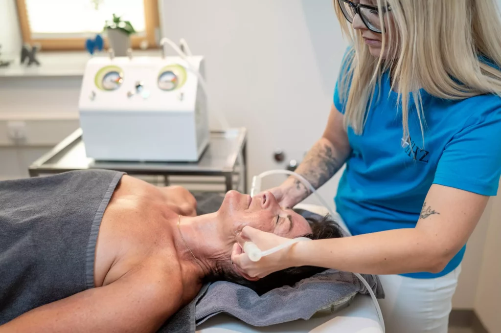 Frau erhält im Gesundheitszentrum Radstadt eine kosmetische Gesichtsbehandlung mit modernem Gerät von Therapeutin im blauen