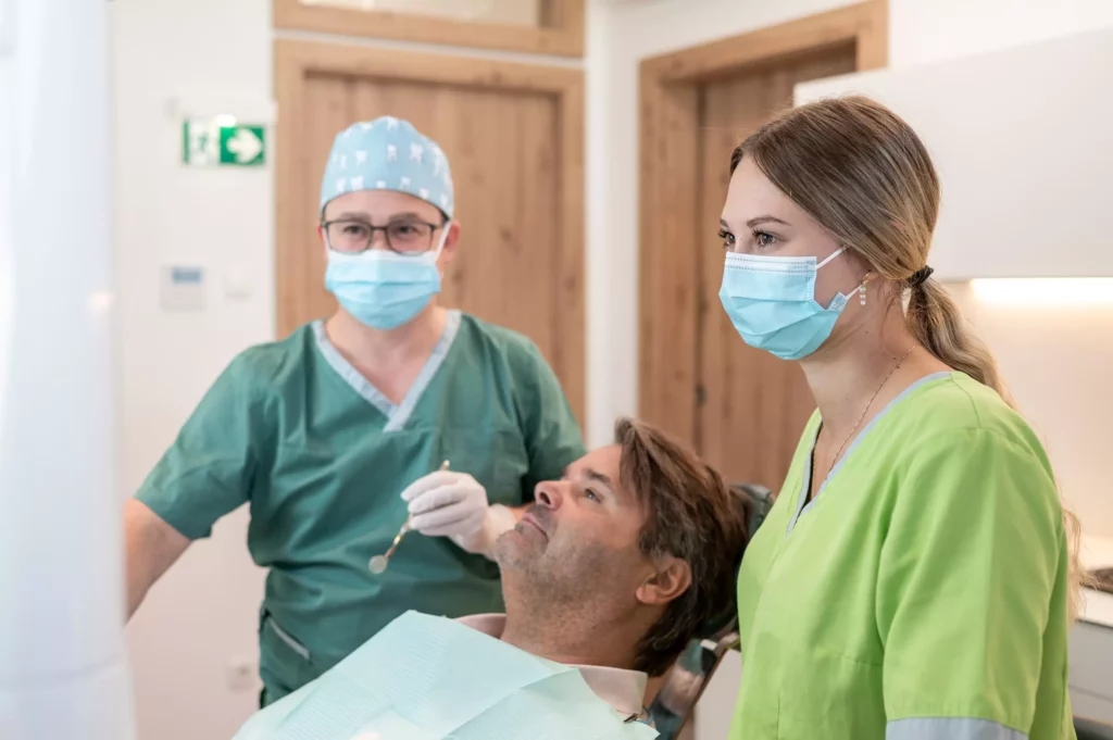Zahnarzt und Assistentin mit Mundschutz untersuchen männlichen Patienten im Behandlungsstuhl in Praxis in Radstadt.