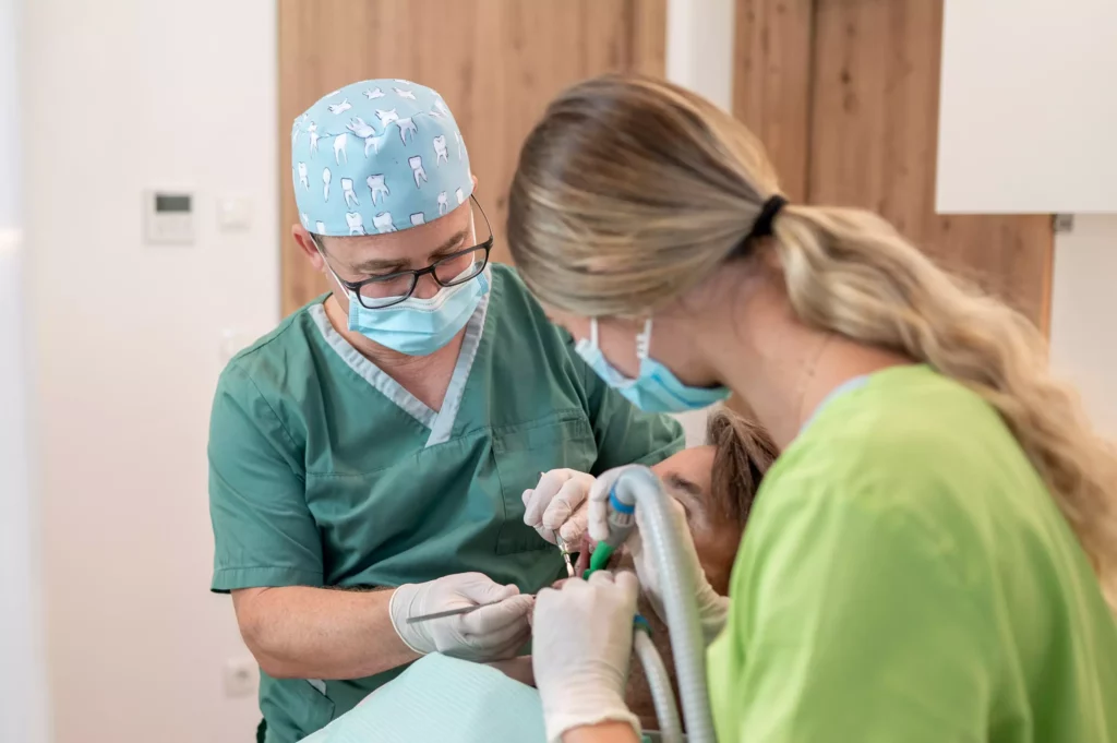 Zahnarzt und Assistentin behandeln Patienten in Praxis in Radstadt mit Mundschutz und Handschuhen bei Kieferchirurgie.