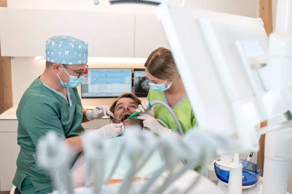 Zahnarzt und Assistentin behandeln Patienten in moderner Zahnarztpraxis mit Röntgenbildschirm im Hintergrund